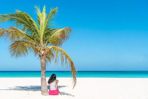 Woman relaxing under a palm tree on a white sand Aruba beach